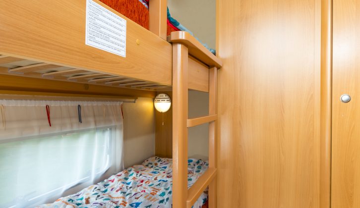 Each bunk has a light and window. The top is accessed by a wooden ladder. The bottom bunk has storage below