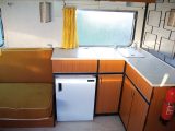 The L-shaped kitchen has a fridge, sink and hob under a hinged worktop, but no oven