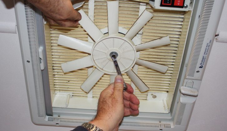 Hold one of the blades to keep the fan still as you undo the securing nut with a spanner