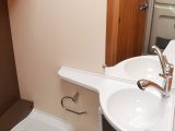 The washroom has a bench toilet and moulded plastic sink unit, the tap serves as a showerhead and the floor comprises the shower tray