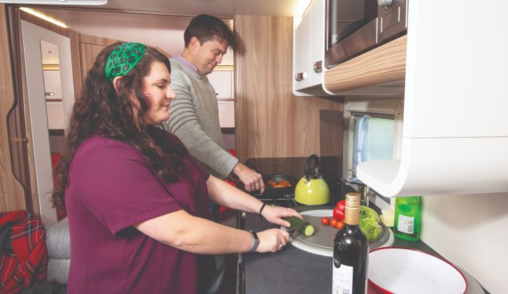 The kitchen worktop is well lit by a window and a striplight and the overhead lockers include crockery and mug racks
