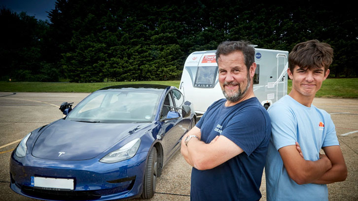 Car towing caravan while father and son stand nearby