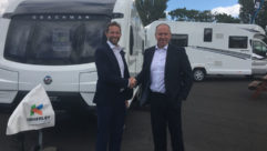 Two men shaking hands in front of a caravan