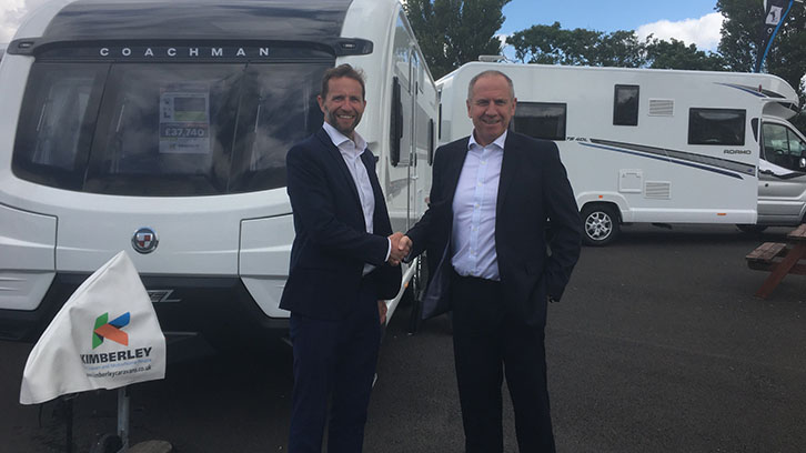 Two men shaking hands in front of a caravan