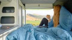 Caravan with sleeping bag as woman drinks tea