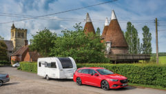 A red car towing a caravan through a village