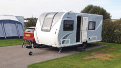 A caravan parked up with a red tow car next to it