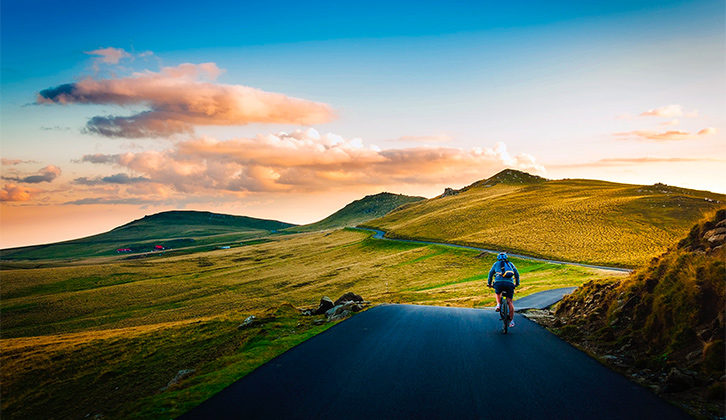 A person cycling along a pathway with a sun set and beautiful countryside ahead of him