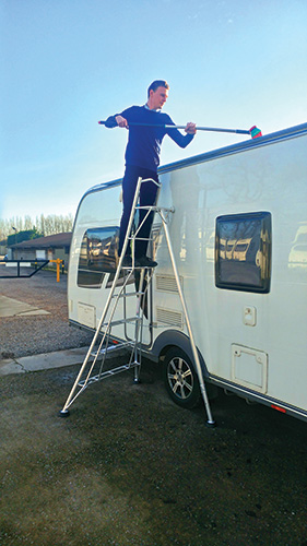 A man standing on a ladder cleaning his caravan
