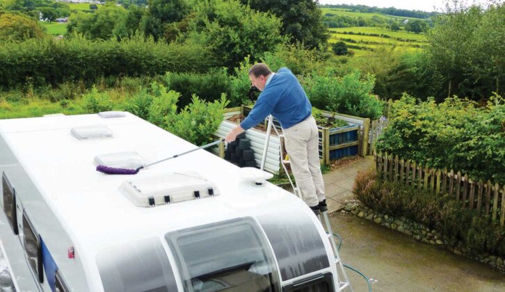 Man on ladder cleaning roof of caravan