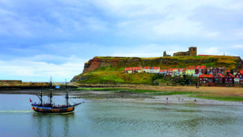 Replica HMS Endeavour in Whitby Harbour, passing the dramatic abbey ruins