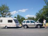 Man on phone by caravan and tow car with bonnet up