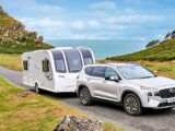 A car towing a caravan with the sea in the background