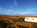 A caravan being towed down a country road during summer with fields on either side