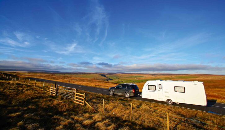 A caravan being towed down a country road during summer with fields on either side