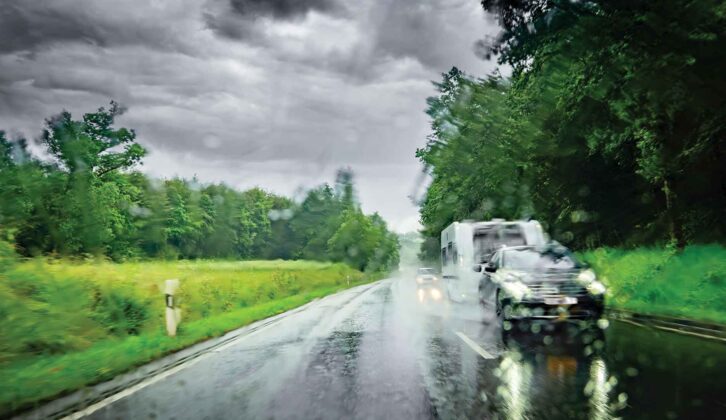 A car towing a caravan driving down a road in the rain