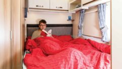 A man sitting up in a bed in a caravan reading a book