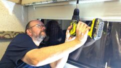 Nigel with a drill in hand in the middle of repairing the blinds