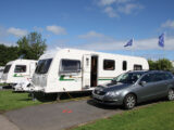 A caravan on a pitch with the tow car parked next to it