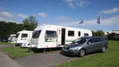 A caravan on a pitch with the tow car parked next to it